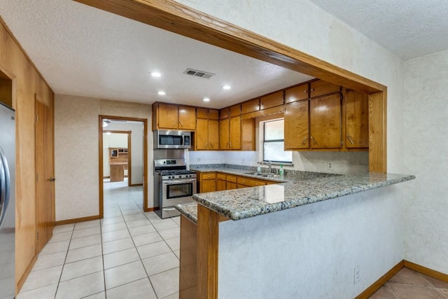 5718 Sheppard Rd, Baytown, TX 77521 - kitchen featuring appliances with stainless steel finishes, a textured ceiling, a sink, brown cabinets, and a peninsula