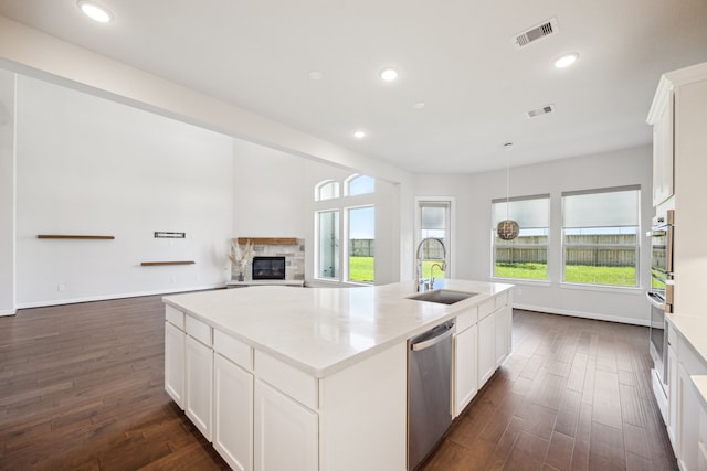 27403 Laurel Bay Ct, Katy, TX 77494 - kitchen featuring dishwasher, a sink, a stone fireplace, a center island with sink, and dark wood-style flooring