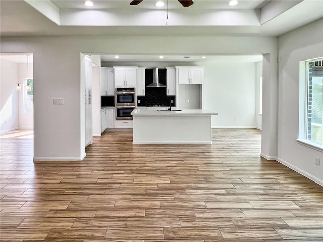 9630 Landry Blvd, Spring, TX 77379 - kitchen featuring wall chimney range hood, stainless steel double oven, light wood-style flooring, a ceiling fan, and white cabinetry