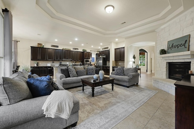 14023 Loramie Creek Ct, Houston, TX 77044 - living area featuring arched walkways, a raised ceiling, light tile patterned flooring, recessed lighting, and a stone fireplace