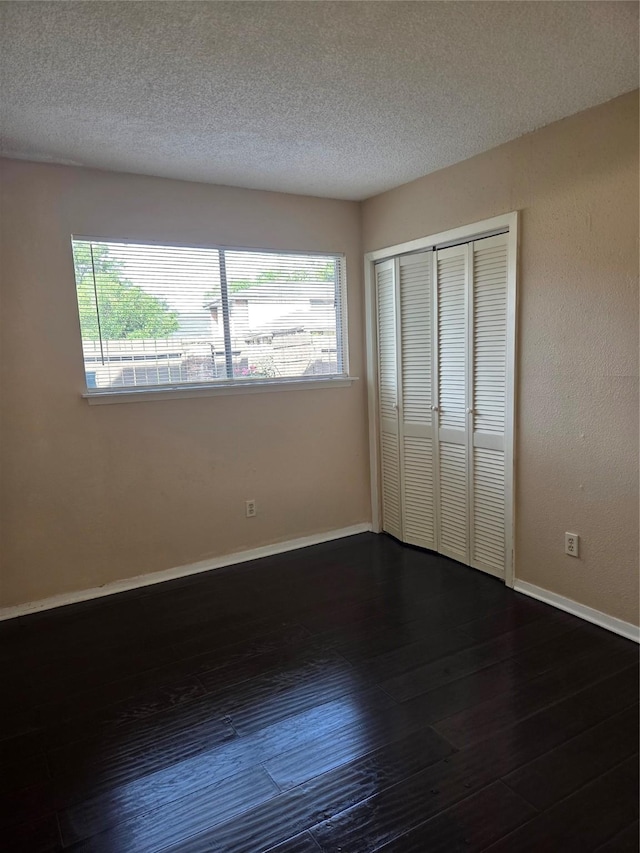 12029 Greenwood Forest Dr, Houston, TX 77066 - unfurnished bedroom featuring multiple windows, dark wood-style flooring, a textured ceiling, a closet, and baseboards