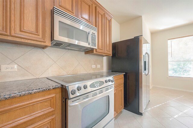 1119 Palmer St, Houston, TX 77003 - kitchen featuring stainless steel appliances, decorative backsplash, dark stone counters, light tile patterned flooring, and baseboards