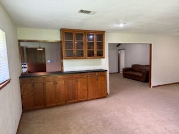 8615 Washington Blvd, Beaumont, TX 77707 - kitchen with brown cabinetry, glass insert cabinets, light carpet, and dark countertops