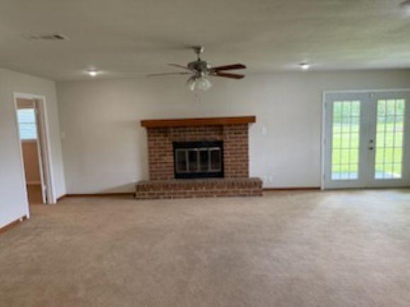 8615 Washington Blvd, Beaumont, TX 77707 - unfurnished living room featuring healthy amount of natural light, carpet, a ceiling fan, and a brick fireplace