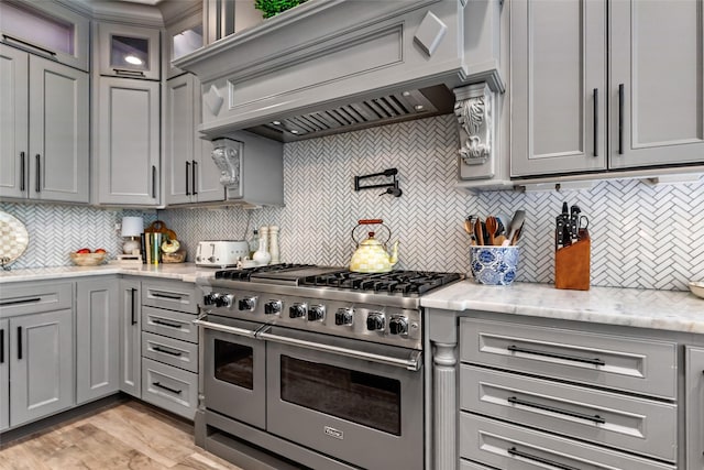 11 Turtle Cove Ct, Kingwood, TX 77346 - kitchen featuring double oven range, gray cabinetry, premium range hood, tasteful backsplash, and light stone counters