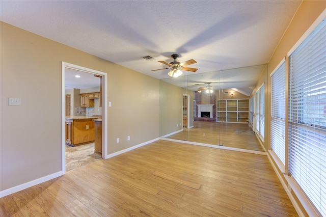 538 Everington Dr, Katy, TX 77450 - unfurnished living room featuring a ceiling fan, light wood-type flooring, a fireplace with raised hearth, baseboards, and a textured ceiling