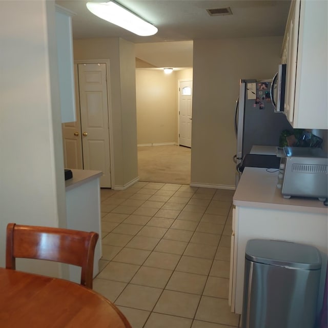 13564 Miller Ln, Willis, TX 77318 - kitchen with light tile patterned floors, white cabinetry, light countertops, stainless steel microwave, and baseboards