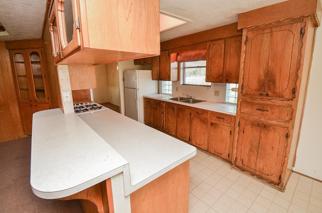346 9th St, Hempstead, TX 77445 - kitchen featuring freestanding refrigerator, light countertops, a sink, brown cabinetry, and a peninsula
