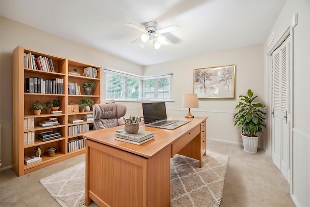 office area with a ceiling fan, light carpet, wainscoting, and a decorative wall