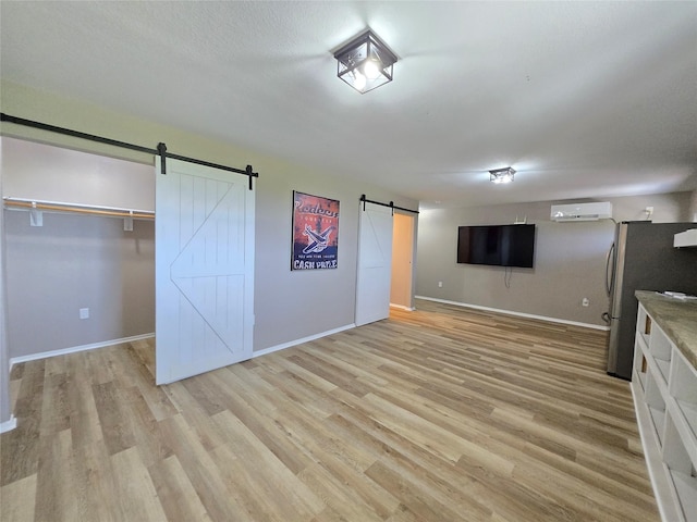 263 Kingfish Ln, Palacios, TX 77465 - interior space featuring a barn door, an AC wall unit, light wood-style flooring, freestanding refrigerator, and baseboards