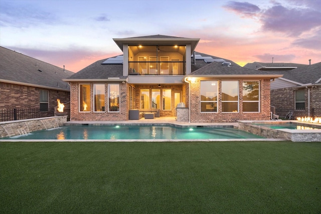19534 Juniper Breeze Ln, Spring, TX 77379 - back of house at dusk with brick siding, a balcony, roof with shingles, and a pool with connected hot tub