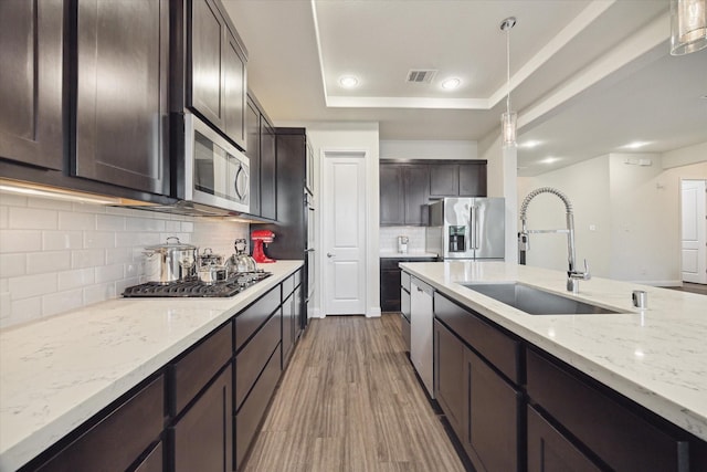 19534 Juniper Breeze Ln, Spring, TX 77379 - kitchen with appliances with stainless steel finishes, a sink, a tray ceiling, dark brown cabinetry, and wood finished floors