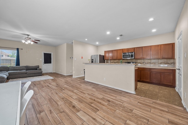 6026 Coleus St, Crosby, TX 77532 - kitchen featuring stainless steel appliances, brown cabinets, light wood-style floors, decorative backsplash, and a ceiling fan