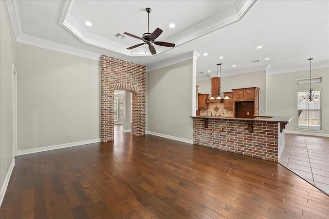 3490 Prescott Dr, Beaumont, TX 77706 - unfurnished living room featuring ceiling fan, a raised ceiling, dark wood-style flooring, crown molding, and a chandelier
