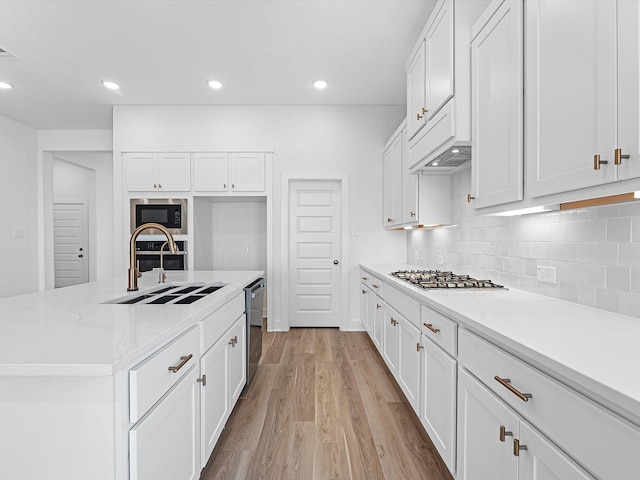 14674 Hereford Grove Ln, Montgomery, TX 77316 - kitchen featuring a sink, appliances with stainless steel finishes, light wood finished floors, white cabinetry, and tasteful backsplash