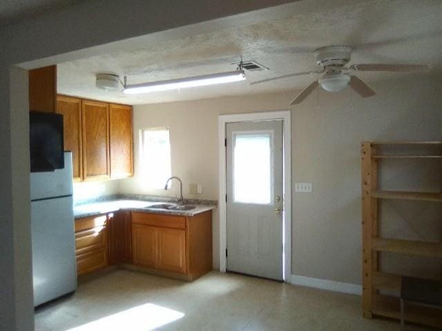 4102 Red Haw Ln, Houston, TX 77022 - kitchen featuring a sink, freestanding refrigerator, brown cabinetry, and a ceiling fan