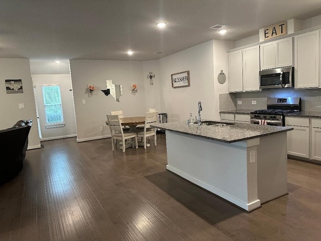 12148 Brazos Dr, Willis, TX 77378 - kitchen with appliances with stainless steel finishes, a sink, dark stone counters, a kitchen island with sink, and decorative backsplash