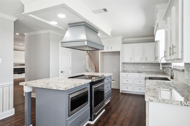 5224 Shorewood Dr, Willis, TX 77318 - kitchen with custom exhaust hood, stainless steel microwave, dark wood-type flooring, white cabinetry, and crown molding