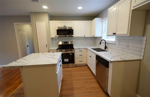 8130 Sharondale Dr, Houston, TX 77033 - kitchen with appliances with stainless steel finishes, a sink, a center island, light stone counters, and light wood finished floors