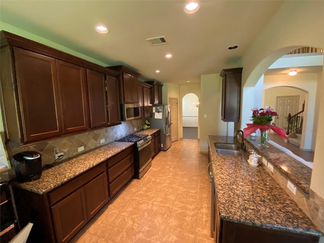 15 S Marshside Pl, Spring, TX 77389 - kitchen featuring appliances with stainless steel finishes, arched walkways, a sink, decorative backsplash, and dark brown cabinetry