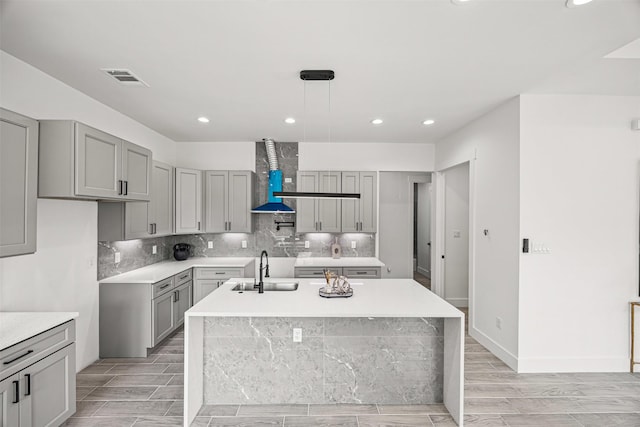 316 E Oakdale St, Dayton, TX 77535 - kitchen featuring a sink, gray cabinets, wall chimney range hood, recessed lighting, and a center island with sink