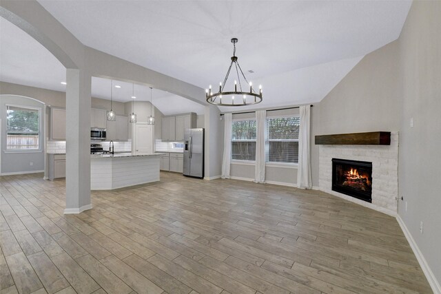 12407 Palo Acebo Ln, Humble, TX 77346 - unfurnished living room with a stone fireplace, light wood-type flooring, a chandelier, baseboards, and plenty of natural light