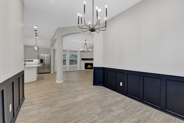 12407 Palo Acebo Ln, Humble, TX 77346 - unfurnished dining area with a chandelier, arched walkways, light wood-style floors, wainscoting, and a warm lit fireplace