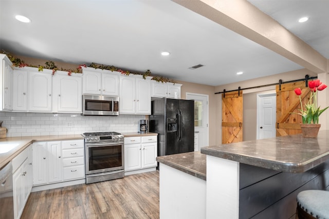 416 State Highway 21 E, Crockett, TX 75835 - kitchen featuring stainless steel appliances, a barn door, white cabinetry, backsplash, and a kitchen bar