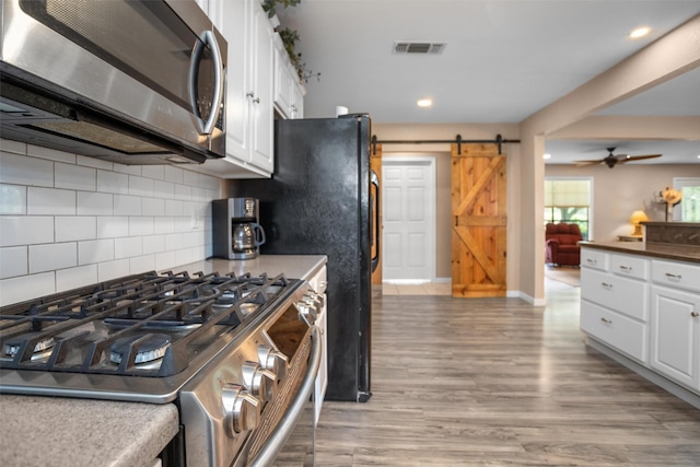 416 State Highway 21 E, Crockett, TX 75835 - kitchen featuring appliances with stainless steel finishes, a barn door, white cabinetry, backsplash, and wood finished floors