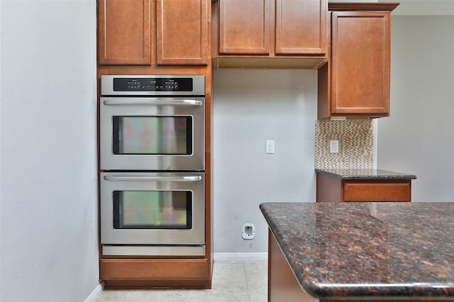 10014 Mahaffey Rd, Tomball, TX 77375 - kitchen featuring stainless steel double oven, baseboards, dark stone countertops, decorative backsplash, and brown cabinetry