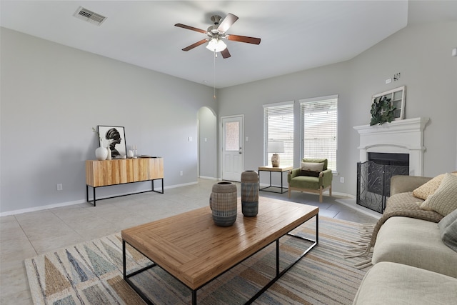 10014 Mahaffey Rd, Tomball, TX 77375 - living room featuring arched walkways, light tile patterned floors, ceiling fan, a fireplace with raised hearth, and baseboards