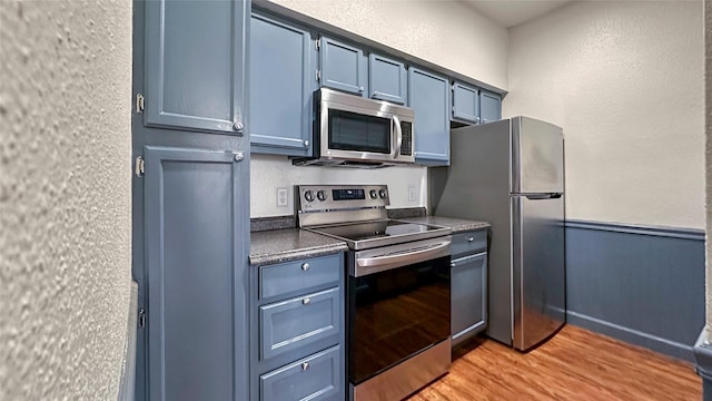 2121 El Paseo St Unit 1511, Houston, TX 77054 - kitchen featuring appliances with stainless steel finishes, light wood-type flooring, blue cabinetry, dark countertops, and a textured wall