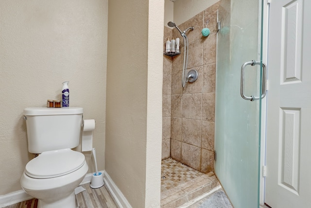 bathroom featuring a shower stall, toilet, wood finished floors, and baseboards