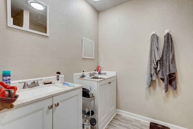 bathroom featuring two vanities, baseboards, wood finished floors, and a textured wall