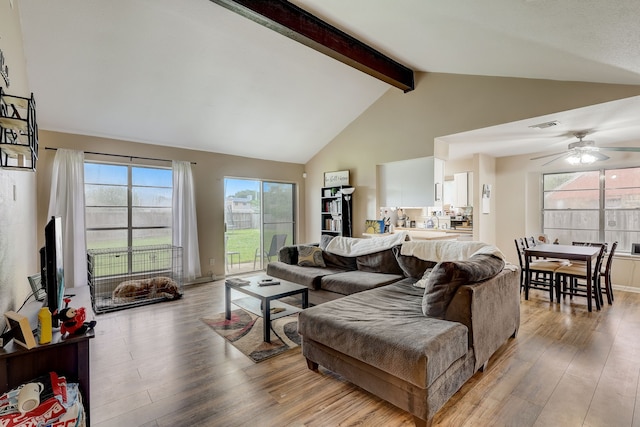 living area with light wood-style floors, beamed ceiling, a ceiling fan, and high vaulted ceiling
