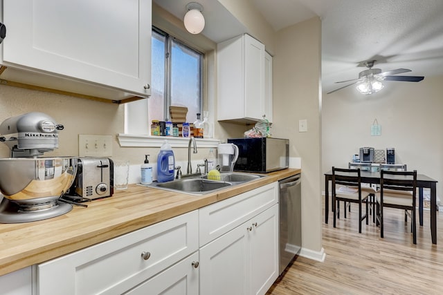 kitchen featuring a sink, butcher block countertops, dishwasher, ceiling fan, and white cabinets