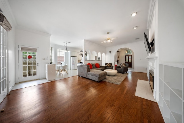 4910 Glen Hollow St, Sugar Land, TX 77479 - living room featuring crown molding, arched walkways, a fireplace with flush hearth, a ceiling fan, and wood finished floors