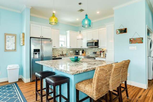 12881 Coronado Dr, Freeport, TX 77541 - kitchen with stainless steel appliances, stacked washer / dryer, light wood-style floors, white cabinets, and a kitchen breakfast bar