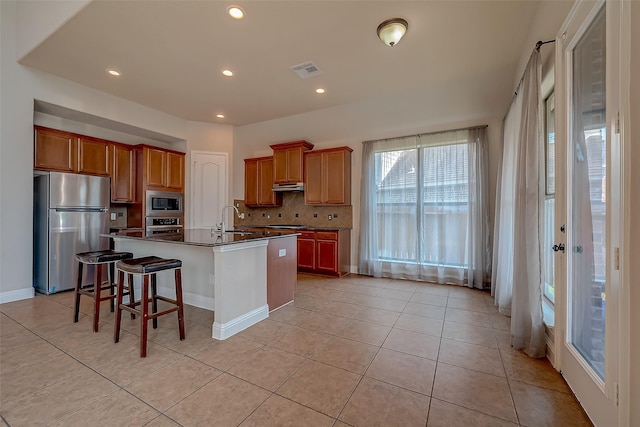 3307 Big Sky Pass, Missouri City, TX 77459 - kitchen with appliances with stainless steel finishes, dark countertops, a kitchen island with sink, tasteful backsplash, and light tile patterned floors