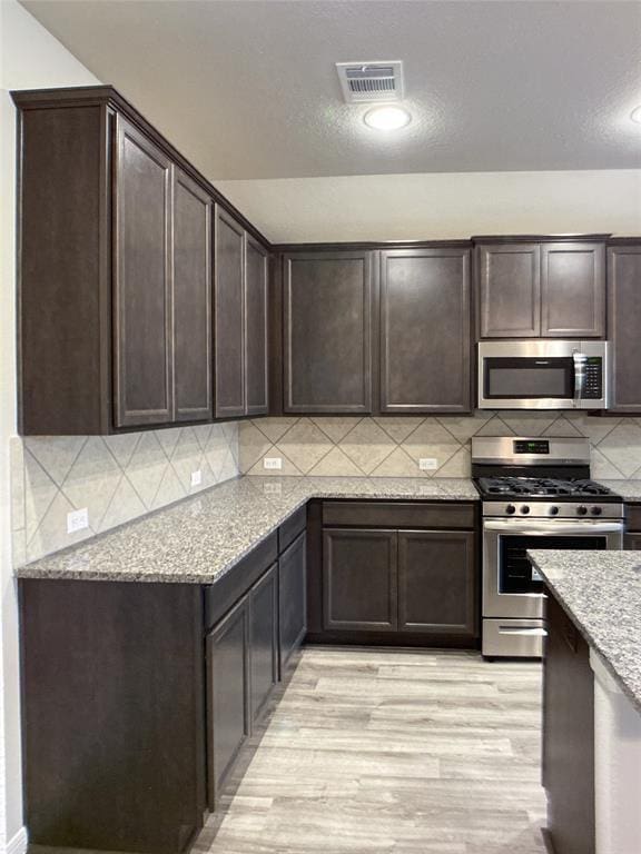 27315 Blue Pool Dr, Katy, TX 77493 - kitchen featuring stainless steel appliances, dark brown cabinetry, light wood-style floors, and light stone countertops