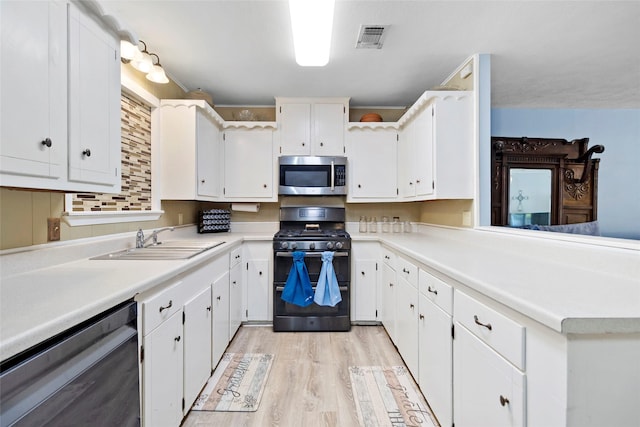 4420 Shady Ln, Huntsville, TX 77320 - kitchen featuring appliances with stainless steel finishes, a sink, white cabinets, light wood-type flooring, and light countertops