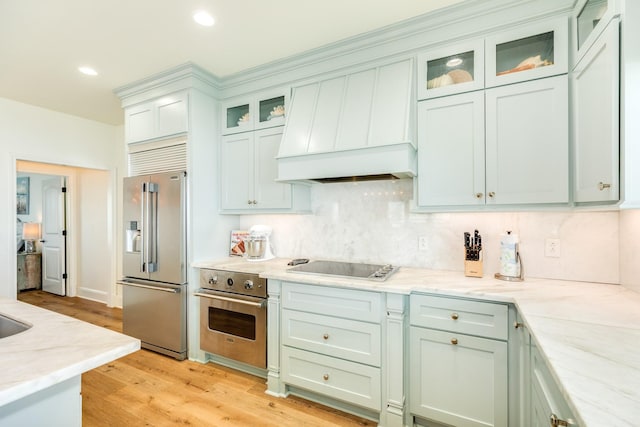998 Austin Dr, Gilchrist, TX 77617 - kitchen with high end refrigerator, oven, black electric stovetop, custom exhaust hood, and light wood finished floors