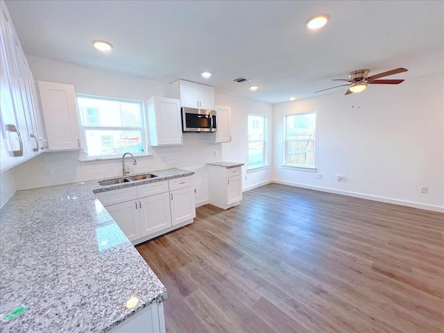 6309 Sandra St, Houston, TX 77028 - kitchen featuring a sink, stainless steel microwave, light stone countertops, decorative backsplash, and white cabinets
