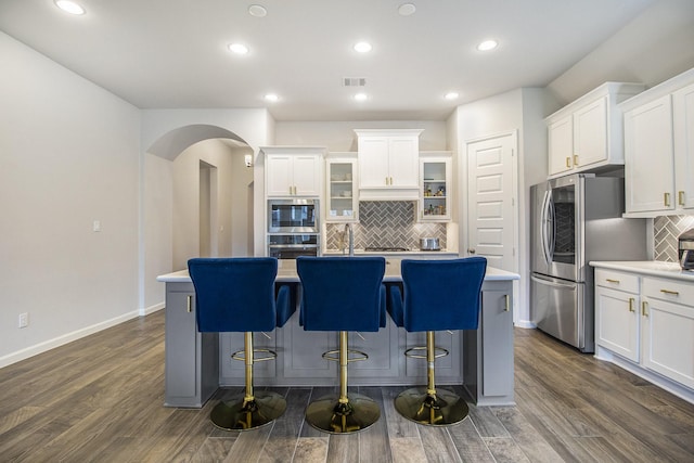 9311 Crescent Mill Dr, Missouri City, TX 77459 - kitchen featuring arched walkways, stainless steel appliances, an island with sink, decorative backsplash, and white cabinetry