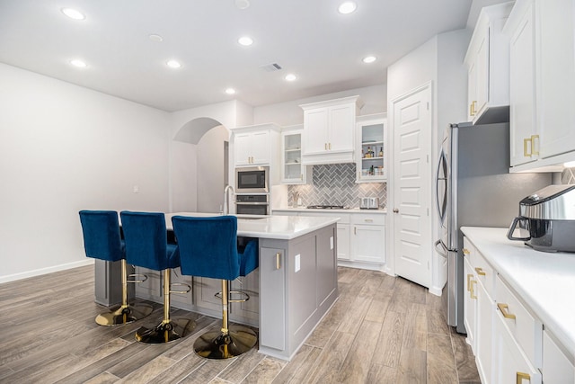 9311 Crescent Mill Dr, Missouri City, TX 77459 - kitchen featuring stainless steel appliances, light wood-style floors, arched walkways, an island with sink, and a breakfast bar