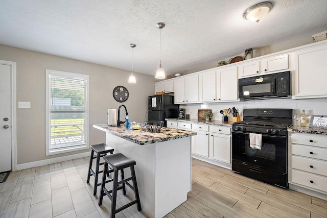715 S Nugent St, La Porte, TX 77571 - kitchen with black appliances, light stone countertops, white cabinetry, a breakfast bar, and a center island with sink