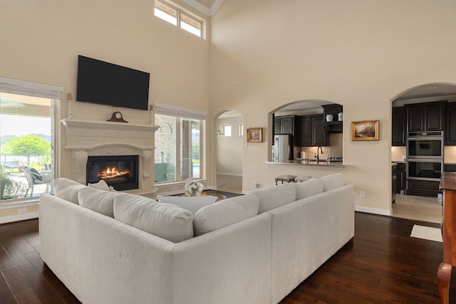 11702 Saporito Way, Richmond, TX 77406 - living area featuring a high ceiling, dark wood-type flooring, a fireplace, baseboards, and arched walkways