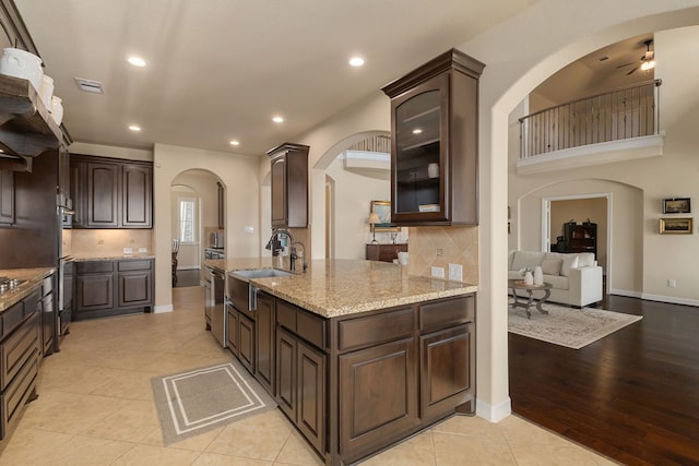 11702 Saporito Way, Richmond, TX 77406 - kitchen featuring a sink, arched walkways, dark brown cabinetry, light stone countertops, and recessed lighting