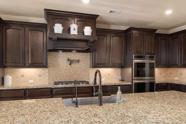 11702 Saporito Way, Richmond, TX 77406 - kitchen featuring stainless steel appliances, a sink, dark brown cabinets, light stone counters, and backsplash