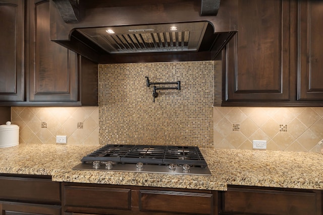 11702 Saporito Way, Richmond, TX 77406 - kitchen featuring exhaust hood, dark brown cabinets, stainless steel gas cooktop, backsplash, and light stone counters